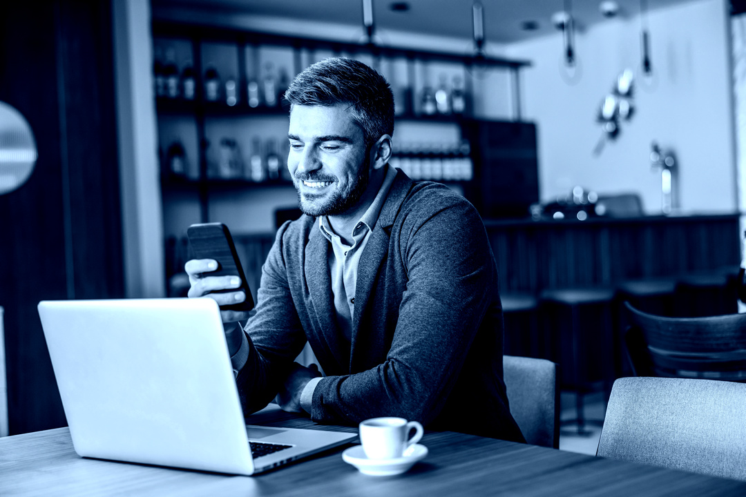 Smiling businessma in a cafe with mobile and tablet devices