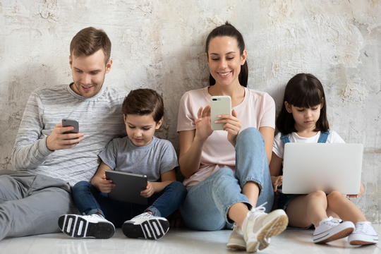Smiling family of four looking at their mobile phones and digital devices