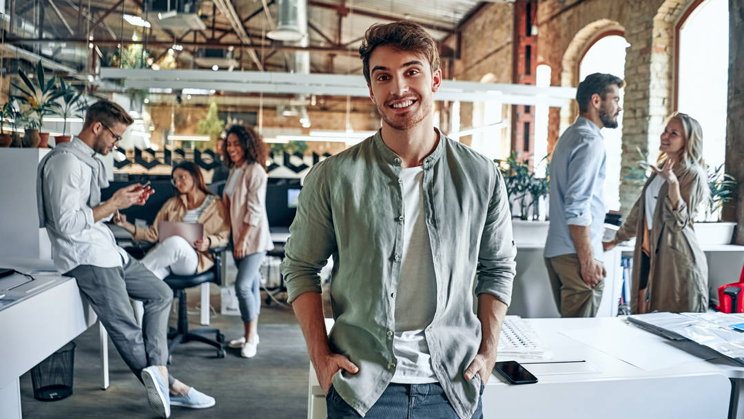 Confident professional standing in modern office workspace with team collaborating in the background