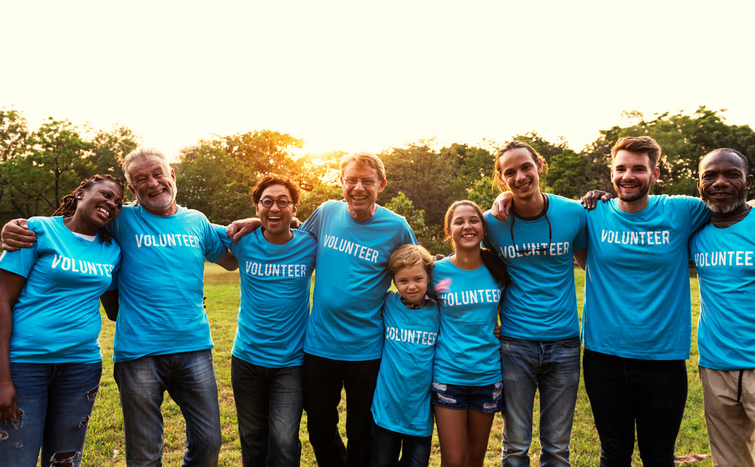 Diverse group of volunteers wearing blue shirts and smiling together outdoors at sunset.